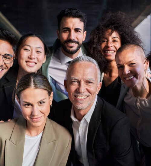 Cheerful portrait of group of businesspeople taking a photo in the office looking at camera smiling. Cheerful portrait of a group of business colleagues taking a photo for the company page in the office, gathered looking at camera smiling, headed by the boss. Startup concept.